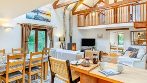 A spacious living area with a high ceiling, wooden beams, a fireplace, a dining table with chairs, and a sofa. - 4 Bed in Torpoint (oc-m30122) (Downderry)