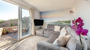 A modern living room with a large sofa, a flat-screen TV, and a view of the sea. - 2 Bed in Llangain (oc-g30185) (Llangain)