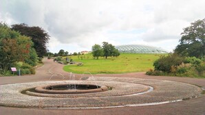 Un bassin circulaire agrémenté d’une fontaine au centre, entouré d’un chemin de gravier.
