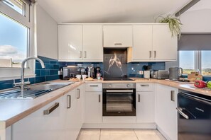 A modern kitchen with white cabinets, a built-in oven, a coffee maker, and a view of the outdoors. - 2 Bed in Llangain (oc-b30186) (Llangain)