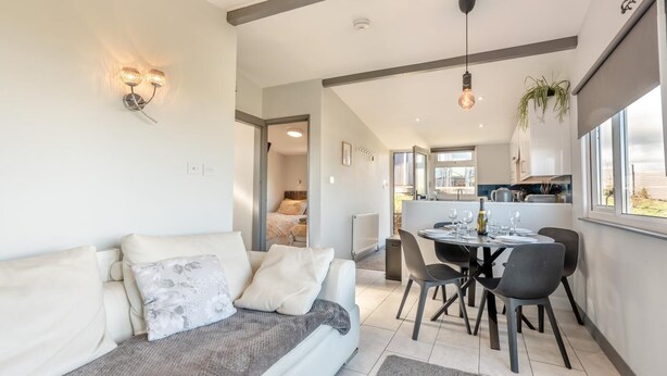 Un salon moderne comprenant un canapé, une table à manger avec des chaises, un coin cuisine et une vue sur l’extérieur.
