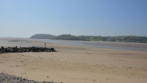 Une plage avec une digue rocheuse, une eau calme et une colline verdoyante à l’horizon.