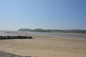 A beach with a rocky breakwater, calm water, and a distant hill with greenery. - 2 Bed in Llangain (oc-b30186) (Llangain)