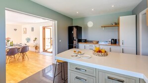 Een moderne keuken met een centraal eiland, een eethoek met tafel en stoelen, en een doorkijk naar de woonkamer.