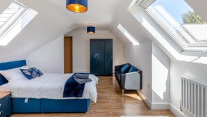 Een slaapkamer met een bed, een kledingkast, een bureau en een stoel. Er zijn dakramen en een raam.