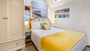Een slaapkamer met een bed, een kledingkast, een dakraam, een boekenplank en een schilderij.