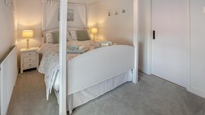A four-poster canopy bed with a white headboard, two bedside tables with lamps, and a door to the right. - 1 Bed in Stibb (oc-c30250) (Stibb)