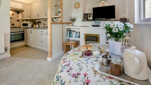 A cozy kitchen with white cabinets, a microwave, and a dining area with a floral tablecloth. - 1 Bed in Stibb (oc-c30250) (Stibb)