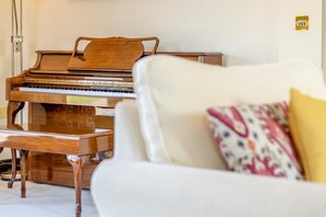 A grand piano in a room with a white armchair and a patterned pillow.