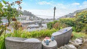 Korbmöbel mit Kissen und einem Tisch, Blick auf eine Stadt mit Gebäuden und einem Gewässer, ferner ein klarer Himmel.