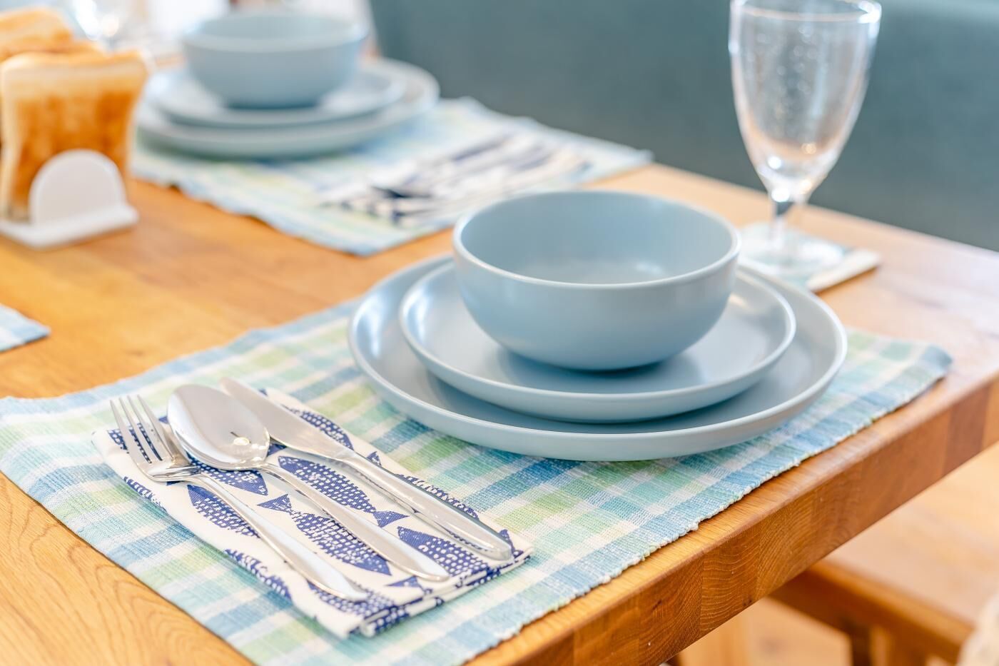 A neatly set dining table with blue plates, a bowl, and cutlery on a striped placemat.