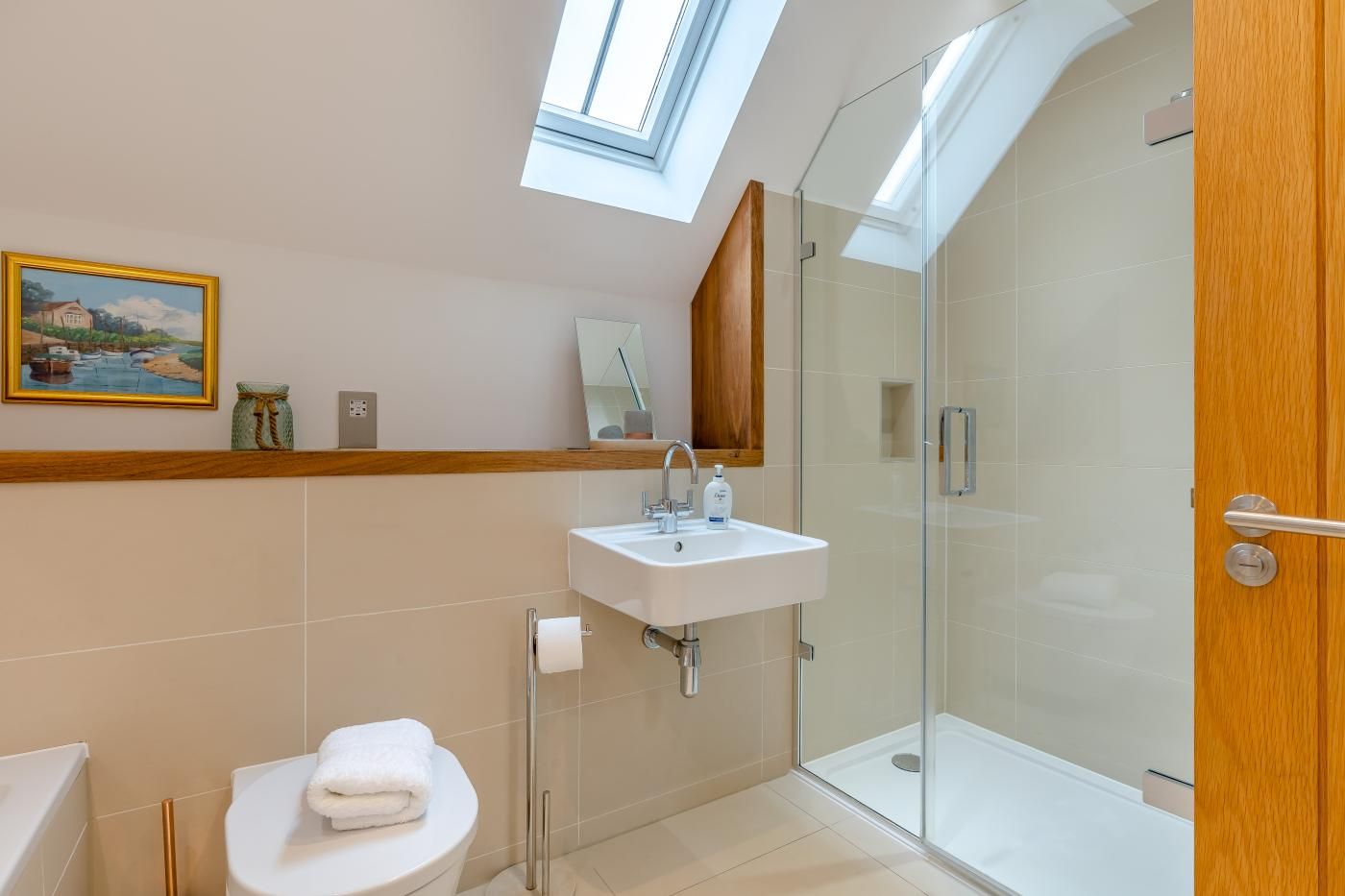 Een moderne badkamer met dakraam, een douchecabine van glas, een wastafel met spiegel en een toilet.