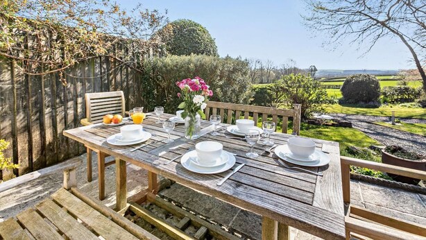 A wooden deck with a table set for breakfast, surrounded by greenery and a view of the countryside. - 2 Bed in North Tamerton (oc-t30362) (North Tamerton)