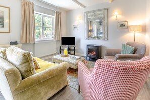 Una sala de estar acogedora con sofá, sillón y reposapiés, chimenea y televisor.