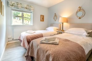 Quarto de hotel com duas camas, uma janela com persianas, um radiador e uma luminária na parede.