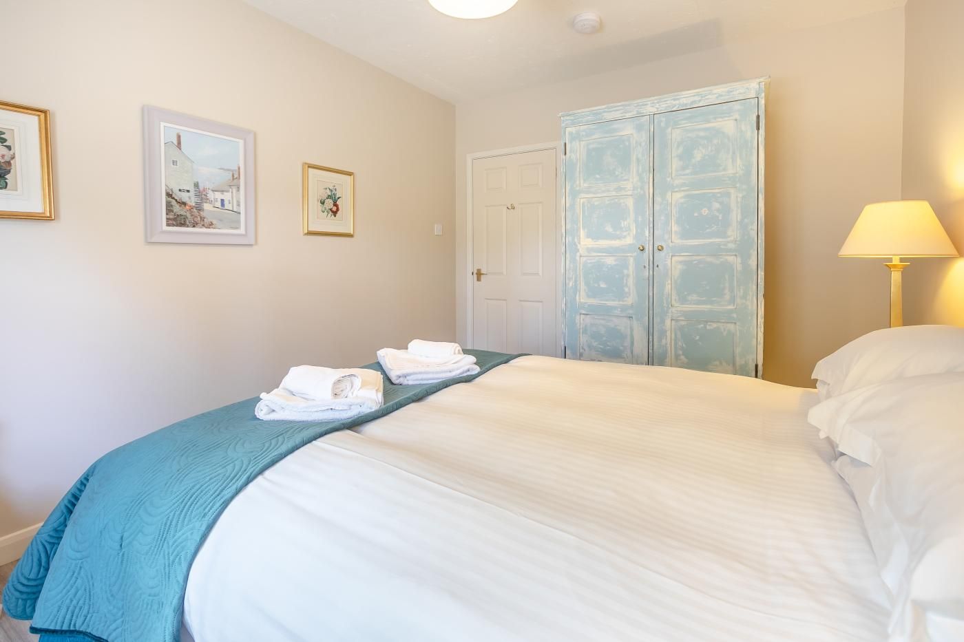 A hotel room with a bed, two towels, a lamp, and a wardrobe.