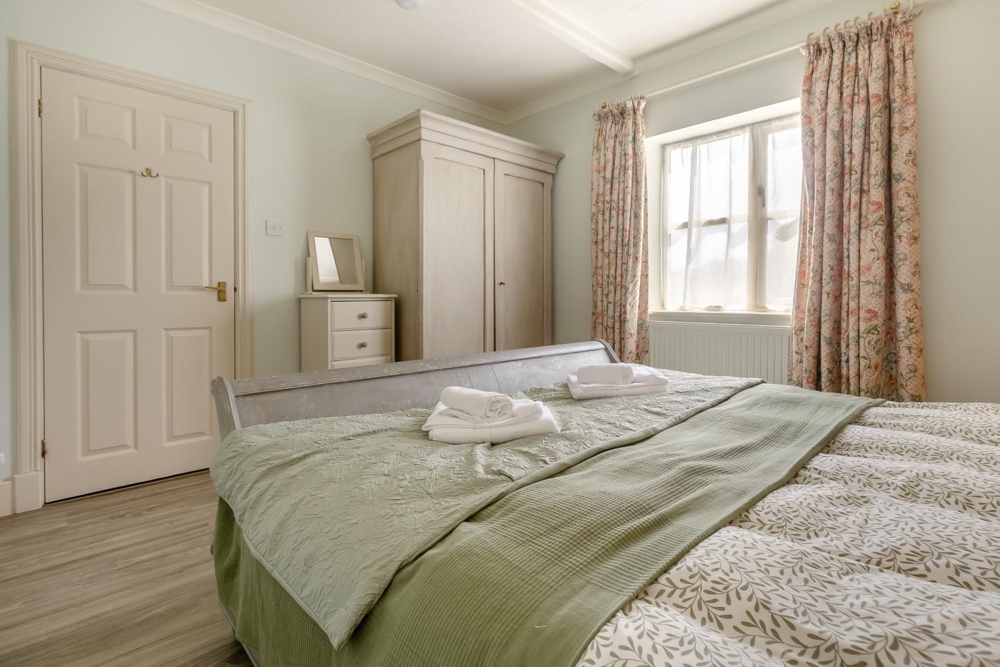 A bedroom with a bed, a dresser, a mirror, and a window with curtains.
