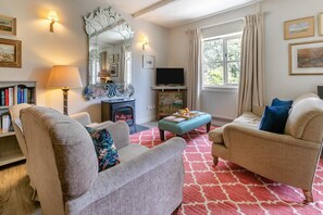 A living room with two armchairs, a sofa, a fireplace, a television, and a large mirror.