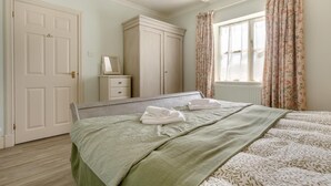 Une chambre à coucher avec un lit, une commode, un miroir et une fenêtre avec des rideaux.