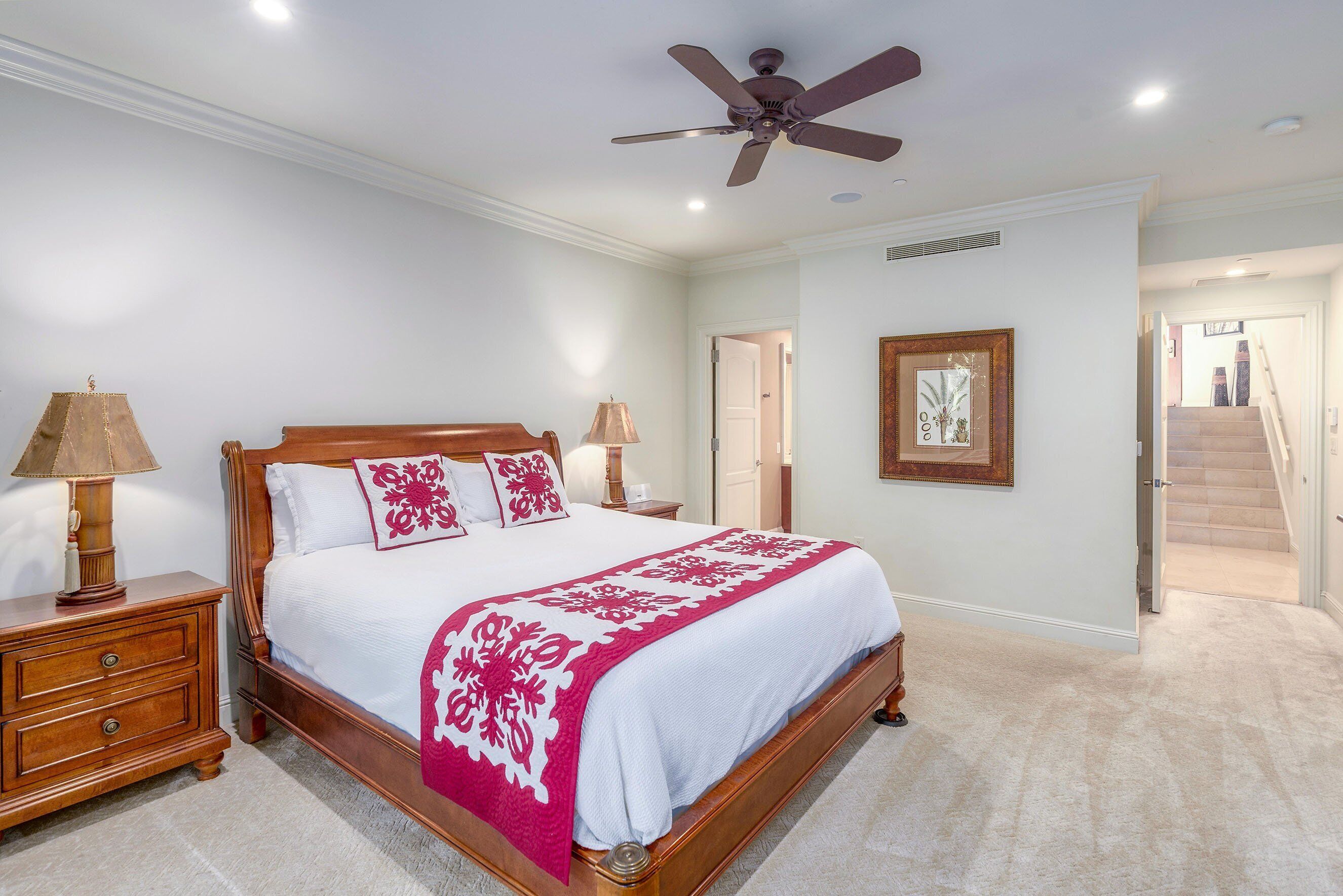 A bedroom with a wooden bed, white walls, a ceiling fan, and a carpeted floor.