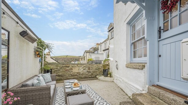 A cozy outdoor seating area with wicker furniture, a patterned rug, and a stone wall backdrop. - 2 Bed in Fowey (oc-r30265) (Fowey)