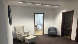 A spacious room with a large grey carpet, a white armchair with a pillow, a grey armchair, and a small ottoman. There is a door leading to a bathroom with a tiled shower area. - Vacation apartment at the clinic Worms (Worms)