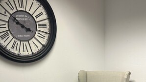 A room with a large wall clock, a light-colored armchair, and a matching ottoman. - Vacation apartment at the clinic Worms (Worms)