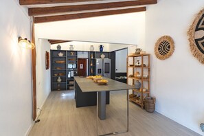 A modern kitchen with a central island, wooden shelves with pottery, and a rustic wall decor. - Villa Son Felip (Palma)