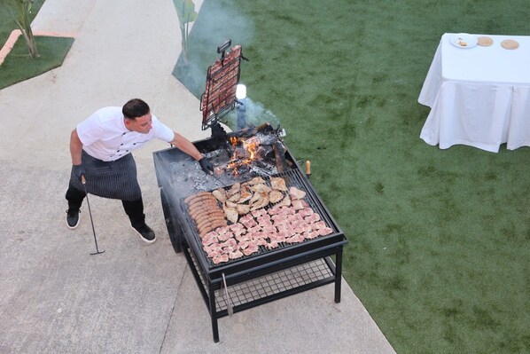 A person grilling food outdoors with a grill and a table with plates in the background. - Villa Son Felip (Palma)