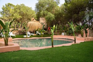 A swimming pool with lounge chairs and a thatched structure in a landscaped garden. - Villa Son Felip (Palma)
