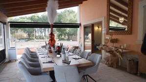 Un'area pranzo riparata con un lungo tavolo apparecchiato per un pasto, posti a sedere all'aperto e vista sul paesaggio circostante.