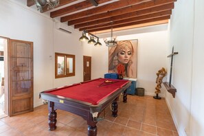 Een kamer met een pooltafel, houten balken in het plafond, een groot kunstwerk in een lijst en een deur met een raam.