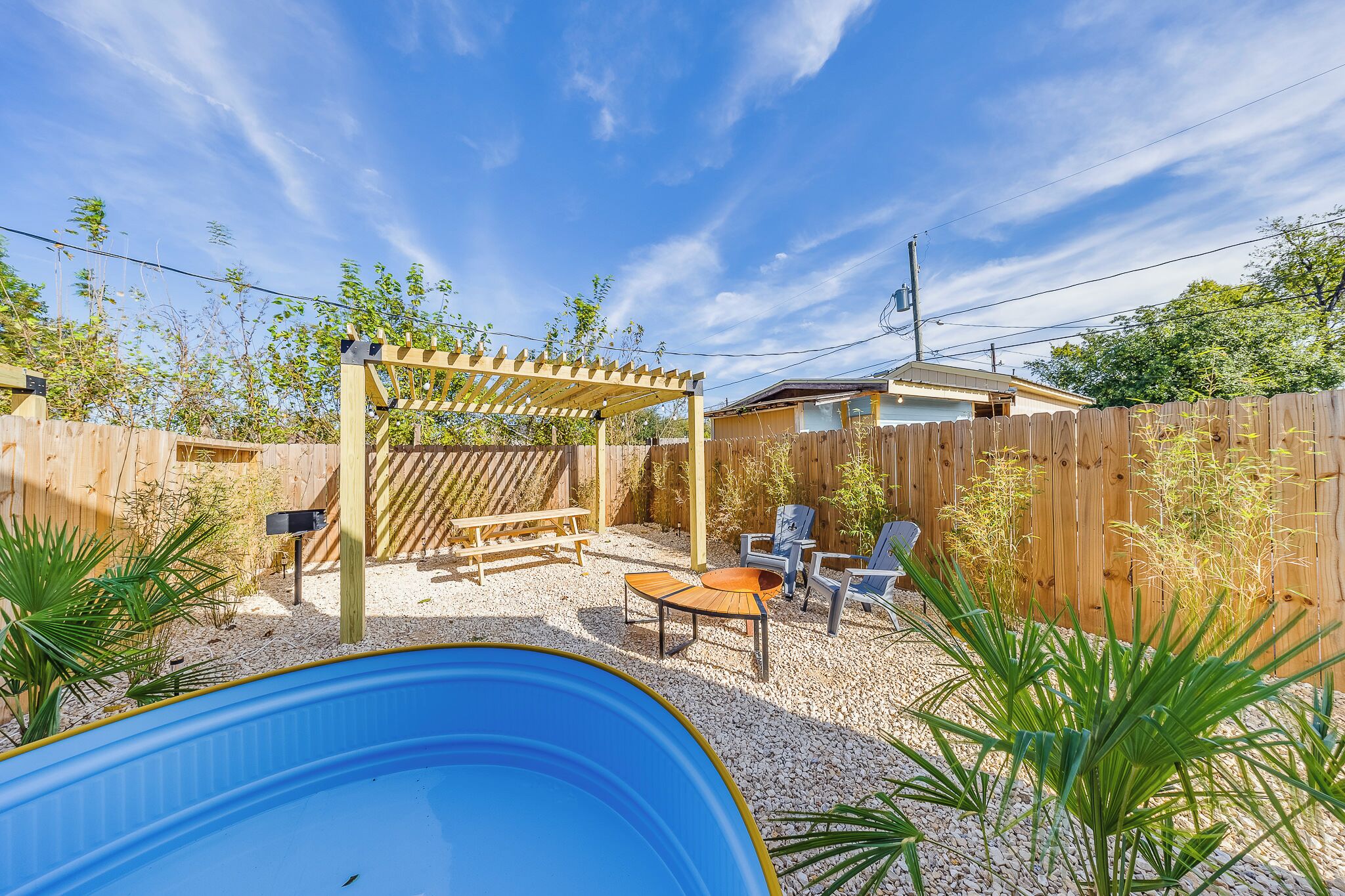 En trädgård med en pergola av trä, en pool, utemöbler och ett staket av trä.