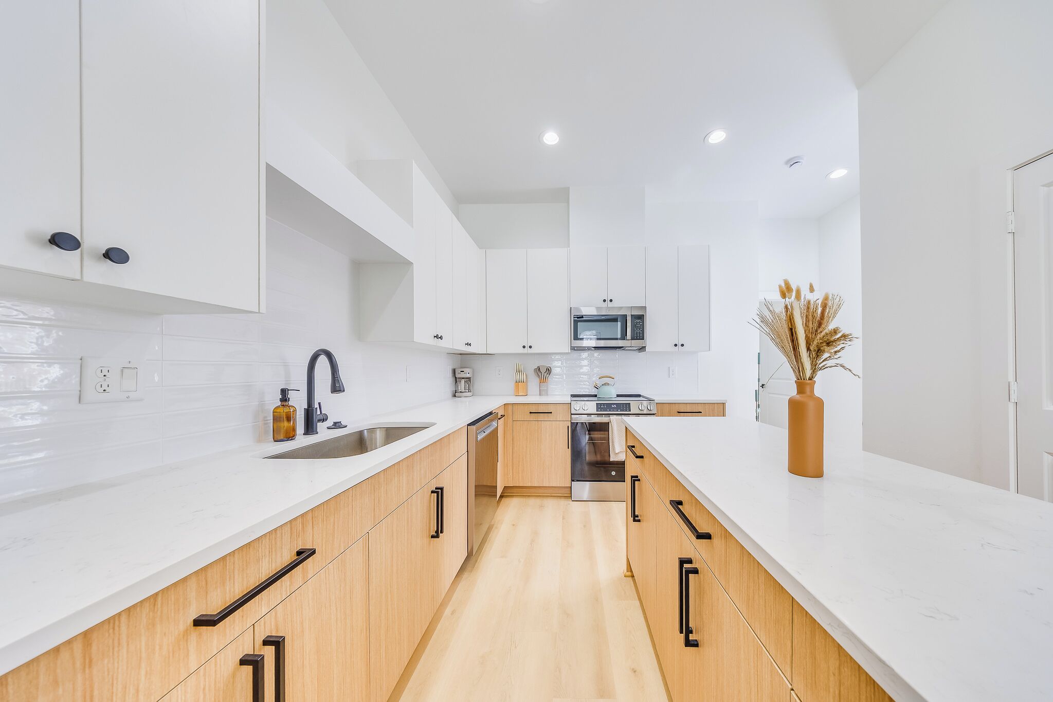 A modern kitchen with white cabinetry, a stainless steel sink, and a microwave.