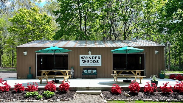 Un edificio rústico de madera con dos mesas de picnic y sombrillas verdes, identificado como "Wonder Woods".