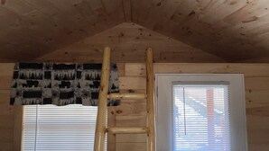 Una habitación con techo de madera, una escalera, una puerta con persianas y una cortina estampada.