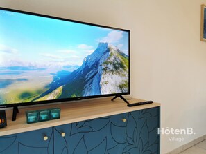 Un téléviseur à écran plat posé sur un meuble en bois, avec vue sur la montagne, une télécommande et trois photophores turquoise.