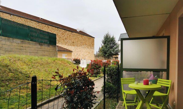 Un balcon avec une table et des chaises, une vue sur un bâtiment en pierre et une clôture verte.