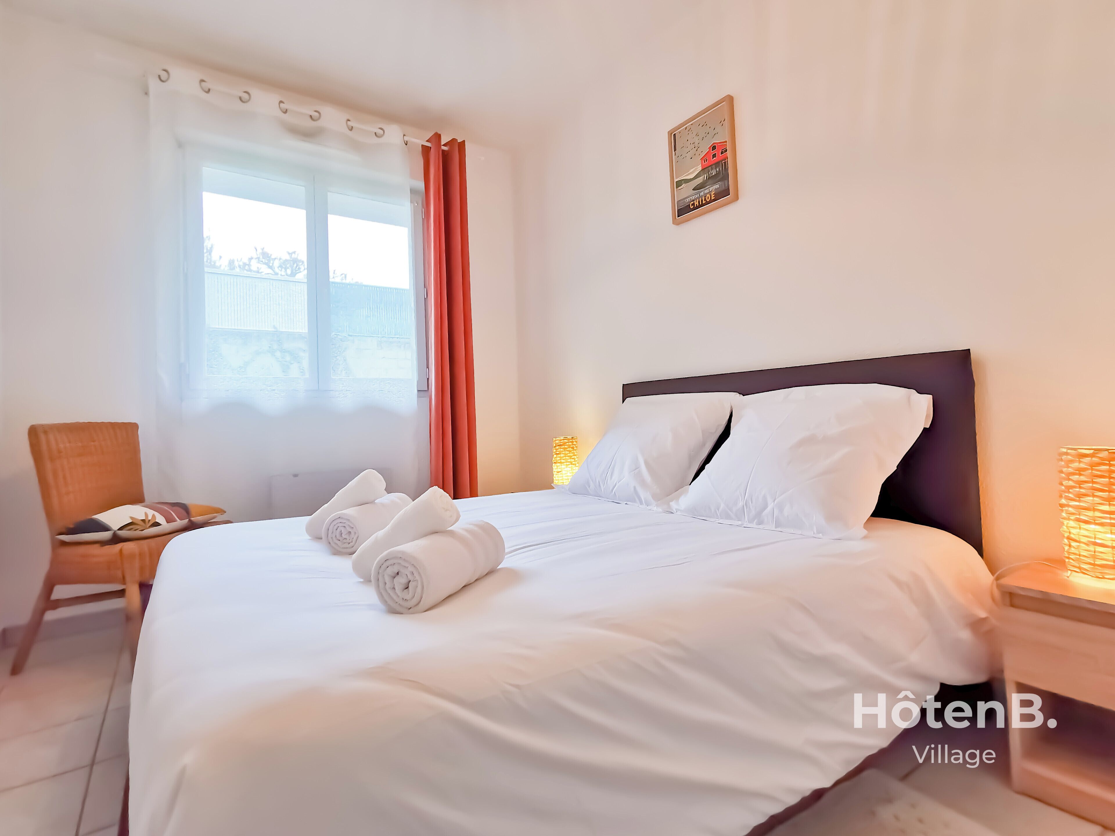 A hotel room with a neatly made bed, a chair, a window with curtains, and a wall-mounted picture.