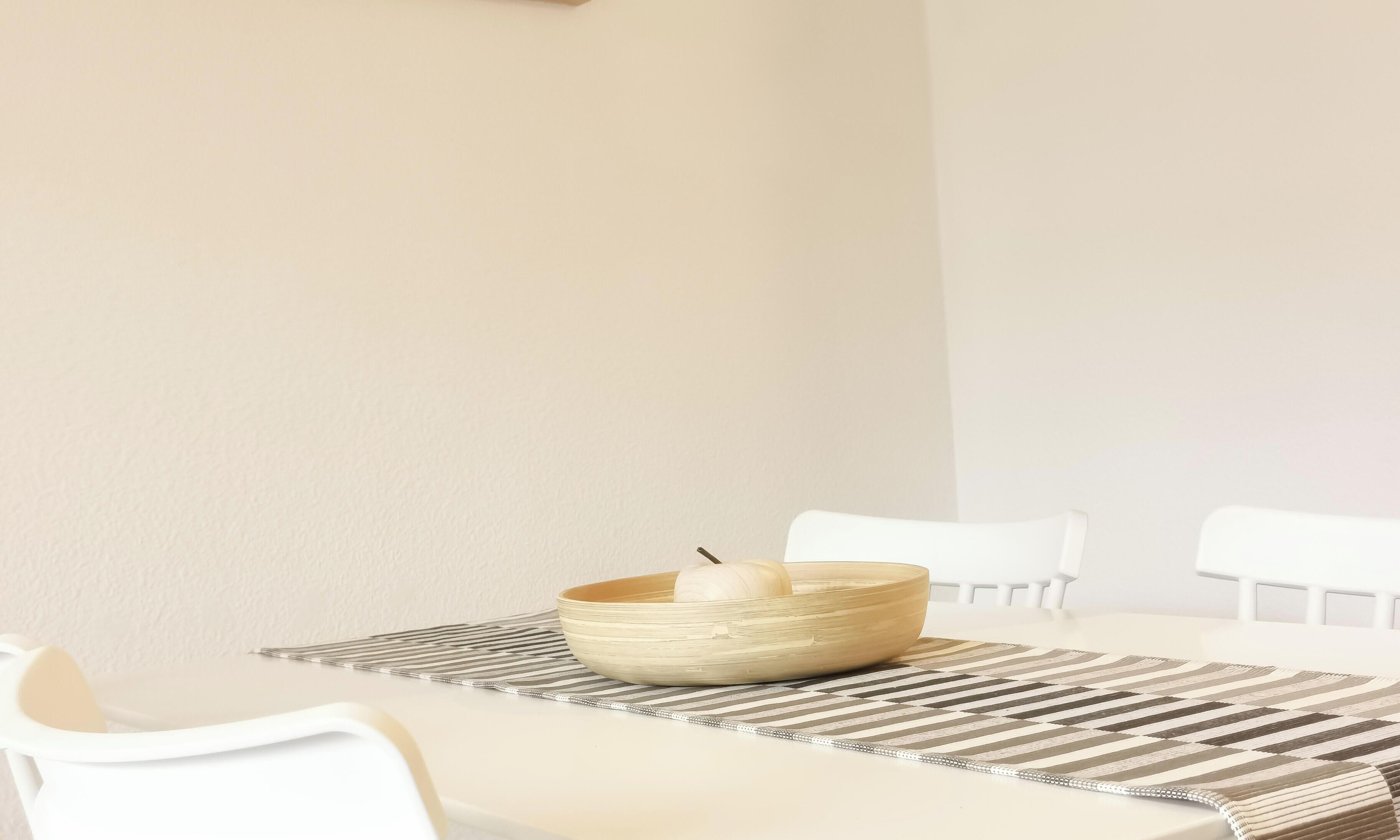 Zona de menjador minimalista amb taula blanca, un bol trenat i un suport de taula a ratlles.
