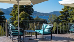 A deck with outdoor furniture, including chairs and a table, overlooking a body of water and hills. - Elektra Hotel (Paleros)