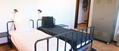 A single bed with a metal frame, a bedside table, a lamp, a wardrobe, and a mirror.