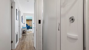 Un pasillo que conduce a un baño con ducha, lavamanos y una silla.