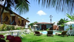 A pool area with lounge chairs and umbrellas, a building with a tiled roof, and a clear sky. - Pousada Gitana (Parnamirim)