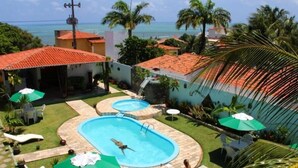 A pool area with two pools, lounge chairs, umbrellas, and a view of the ocean. - Pousada Gitana (Parnamirim)