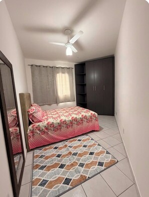 A bedroom with a bed, a ceiling fan, a wardrobe, and a mirror. - Apartment facing the beach in Aviação, Praia Grande (Praia Grande)