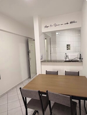 A dining area with a wooden table and four chairs, a kitchen with white tiles, and a door leading to another room. - Apartment facing the beach in Aviação, Praia Grande (Praia Grande)
