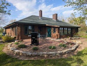 Eine Blockhütte mit Schornstein, eine Terrasse mit Grill und ein Steinrand um den Garten.