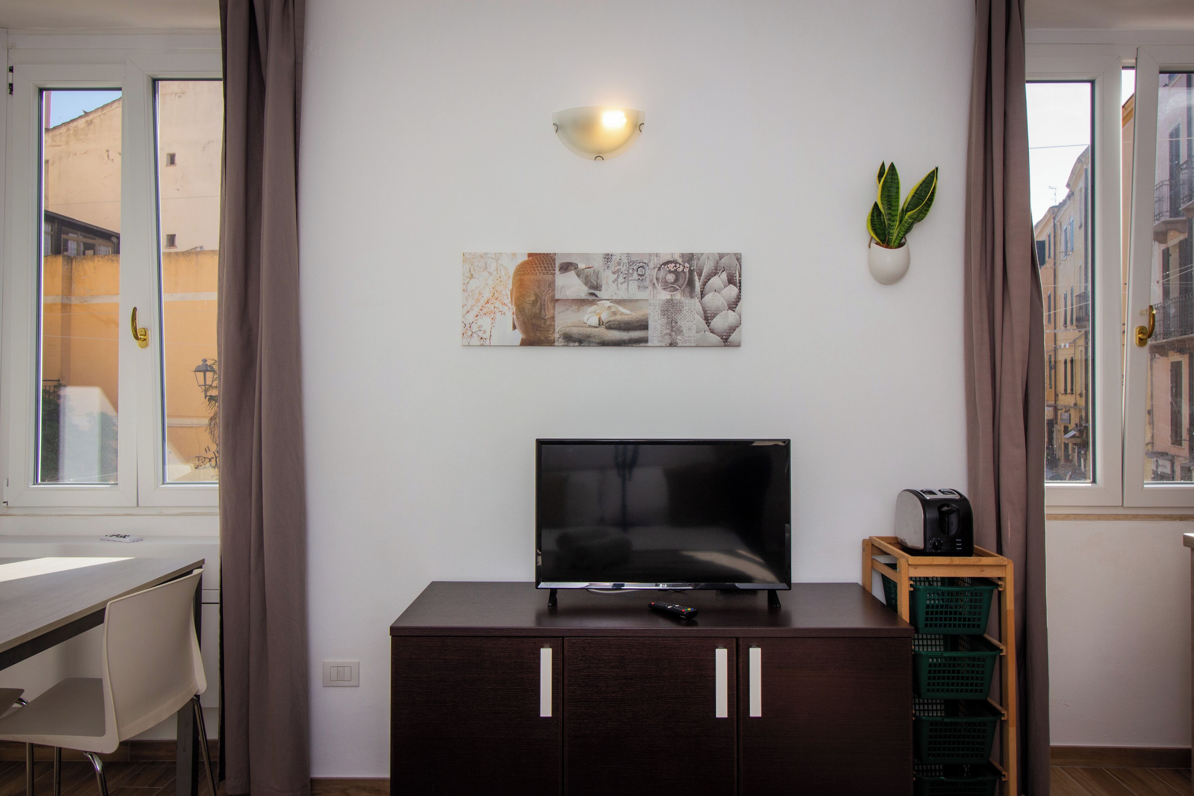 Een moderne woonkamer met een flatscreen televisie op een houten kast, een wandlamp en een potplant.
