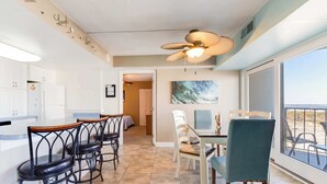 Uma sala de jantar com mesa e cadeiras, um ventilador de teto e vista pela uma grande janela.